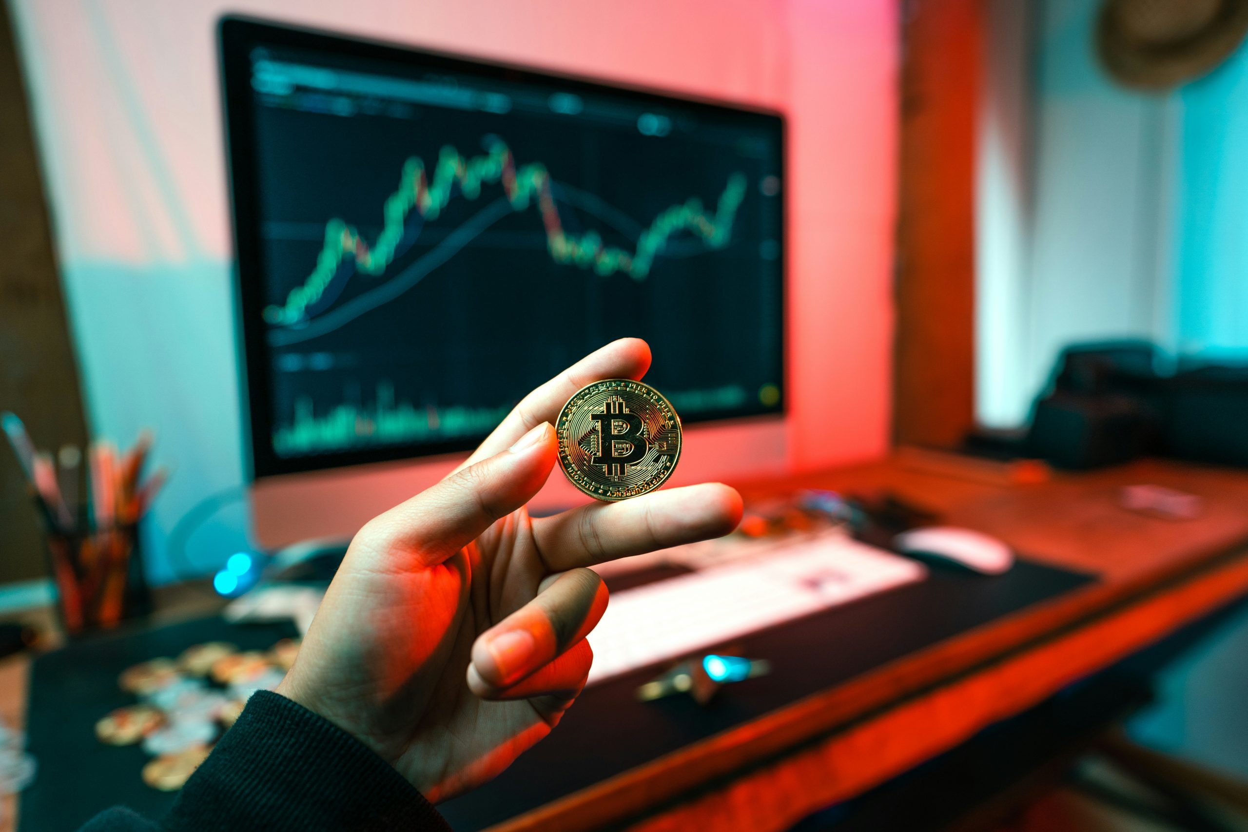 Bitcoin coin held in front of a trading chart