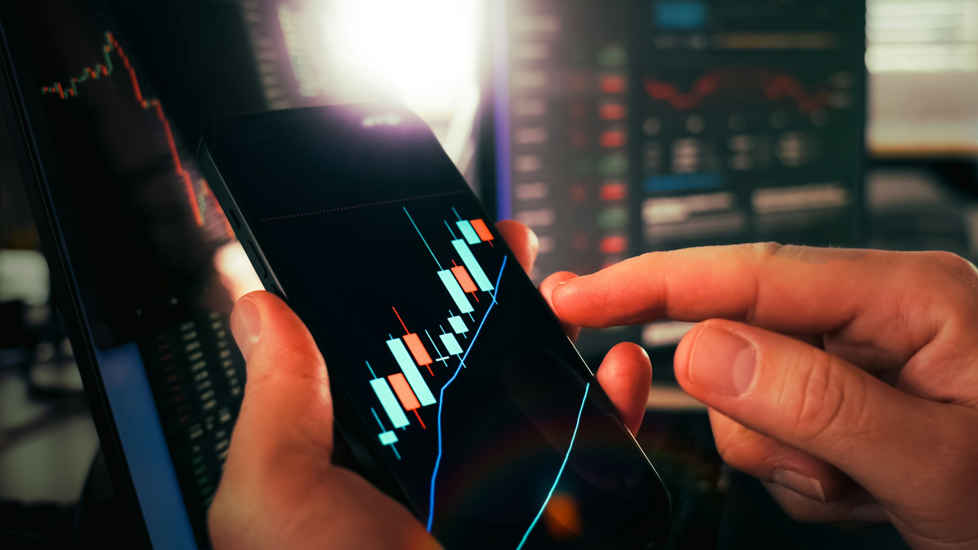 Hands holding a smartphone displaying financial market charts, illustrating tokenized stocks used as collateral on Aave V4