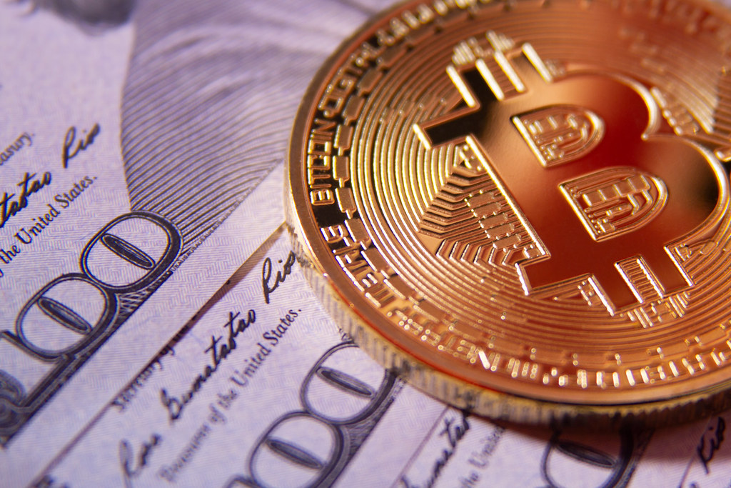 A physical Bitcoin token resting on fanned United States dollar bills, illustrating institutional Bitcoin ETF flows