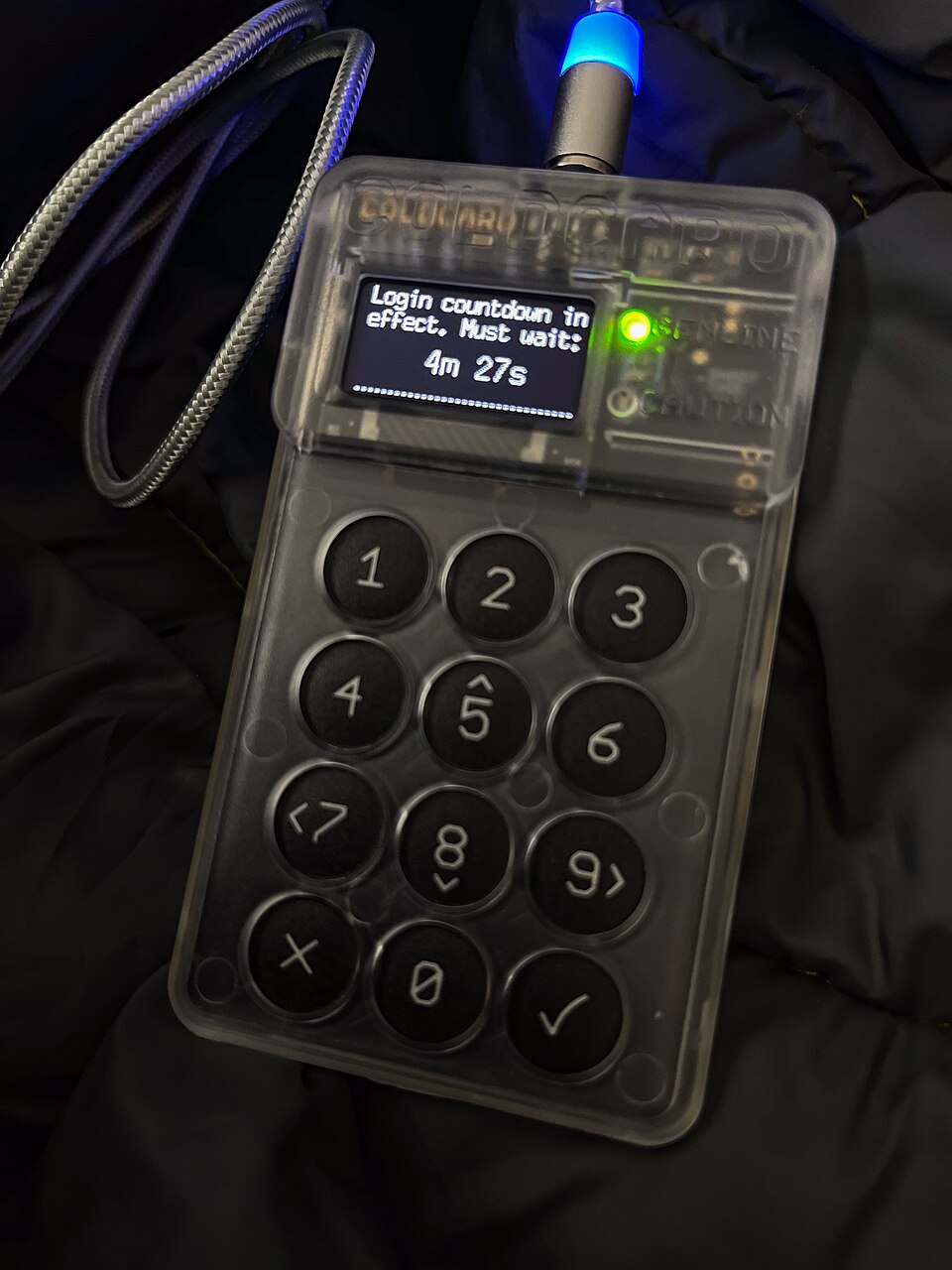 A Coldcard cryptocurrency hardware wallet beside a phone displaying a login countdown